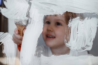 Çocuk cam bir tahtaüzerine beyaz bir boya çizer. Simüle ekran. Fırça ile mutlu çocuk