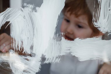 Çocuk cam bir tahtaüzerine beyaz bir boya çizer. Simüle ekran. Fırça ile mutlu çocuk