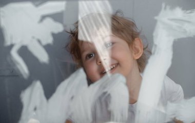 Çocuk bir cam tahta üzerinde beyaz boya ile güneş çizer. Simüle ekran. Mutlu çocuk