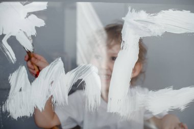 Çocuk bir cam tahta üzerinde beyaz boya ile güneş çizer. Simüle ekran. Mutlu çocuk