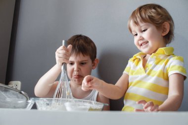 İki mutlu küçük çocuk kısa ekmek yapıyor. Gülerek eğleniyorlar ve hamuru karıştırdılar. Tatlıların hazırlanması.