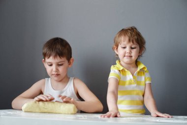 Küçük neşeli çocuklar ekmek yapar. Beyaz bir masada bir oklava ile hamur dışarı rulo. Tatlının hazırlanması