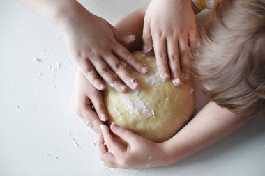 Yakından kapatın. Dört çocuğun eli, hamuru beyaz masaya bastırıyor. Tatlıların hazırlanması.