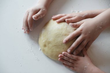 Yakından kapatın. Dört çocuğun eli, hamuru beyaz masaya bastırıyor. Tatlıların hazırlanması.