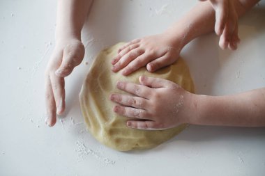 Yakından kapatın. Dört çocuğun eli, hamuru beyaz masaya bastırıyor. Tatlıların hazırlanması.
