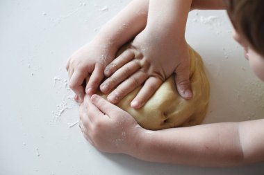 Yakından kapatın. Dört çocuğun eli, hamuru beyaz masaya bastırıyor. Tatlıların hazırlanması.