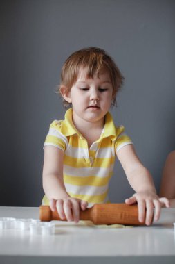 Küçük sevimli kız shortbread yapıyor. Beyaz bir masada bir oklava ile hamur dışarı rulo. Tatlının hazırlanması