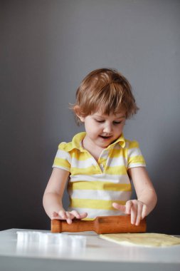 Küçük sevimli kız shortbread yapıyor. Beyaz bir masada bir oklava ile hamur dışarı rulo. Tatlının hazırlanması