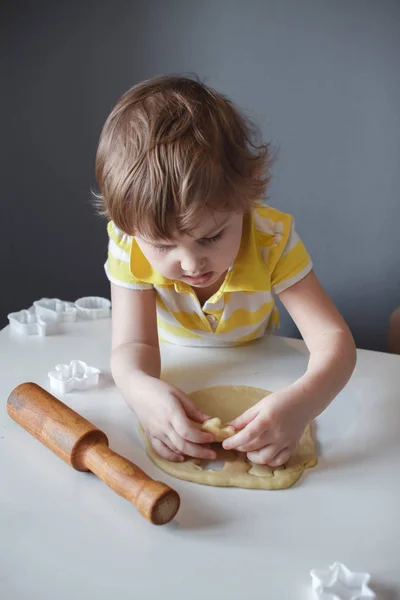 The child makes cookie molds on a white table. Preparation of homemade dessert