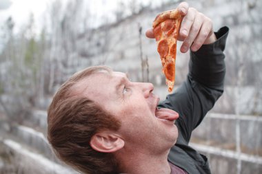 Adam pizza yiyecek. Açık havada. Elinde bir parça pizza tutuyor, yakın çekim. lezzetli yemek