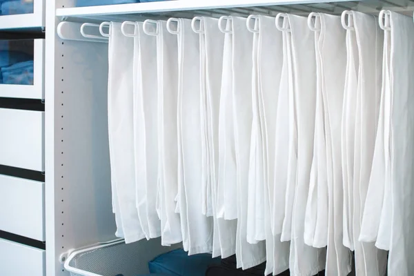 Storage of things in the closet and order in the house. White things neatly hanging on a hanger for trousers.
