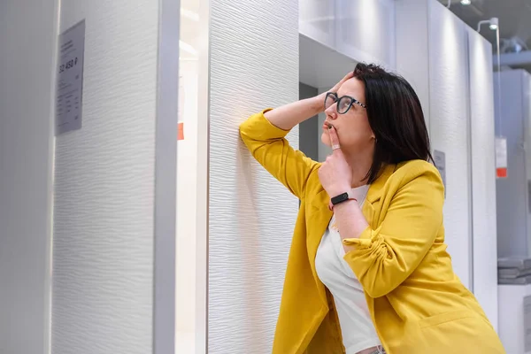 Aankoop van meubels. Een meisje in een geel jasje kiest een witte garderobe in een meubelwinkel. Kledingkast voor kleding opslag. — Stockfoto