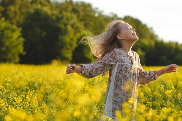 健康と若者の概念。ケアフリー若い女の子は、菜の花畑で夕日を楽しんでいます. ストック画像