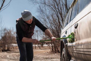 Bir adam dışarıda beyaz, kirli arabayı yıkar. Araba bakımı