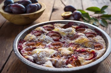 Ahşap bir arka planda kasede erik turtası ve taze erikler..