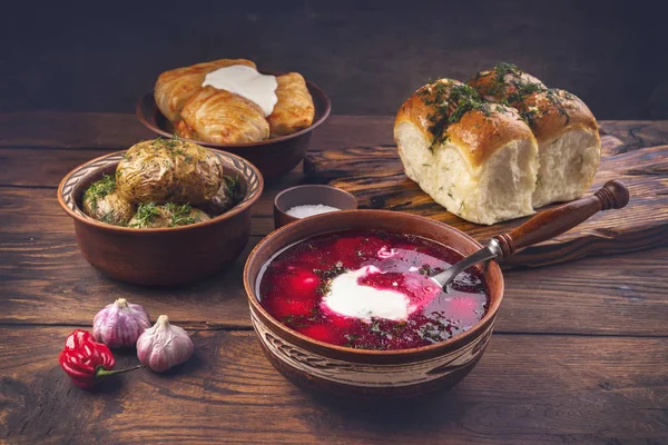 Ukrainian national cuisine - a bowl with borsch, donuts with garlic, cabbage rolls, baked potatoes on a dark wooden background. Processing photos with toning.