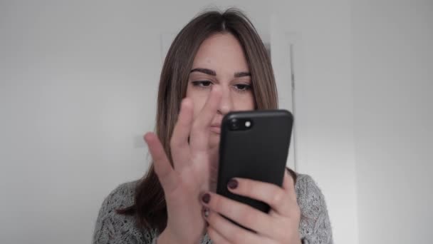 Крупним планом портрет красивої молодої брюнетки посміхається, використовуючи на смартфоні вдома — стокове відео