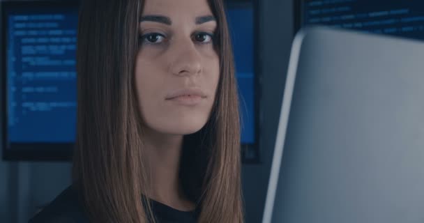 Portret van een jonge vrouw hacker programmeur kijken camera in het datacenter gevuld met schermen — Stockvideo