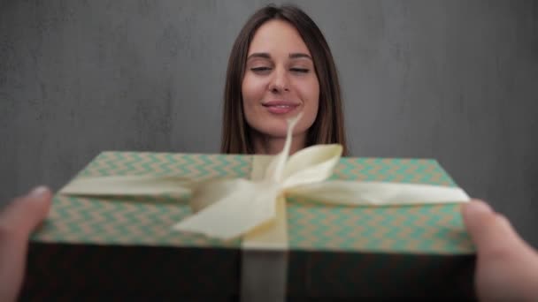 Μια νεαρή γυναίκα στέκεται περιμένοντας μια έκπληξη, γυρίζοντας το κεφάλι της, βλέπει ένα κουτί με ένα δώρο. γκρι φόντο, αργή κίνηση. 4K. — Αρχείο Βίντεο
