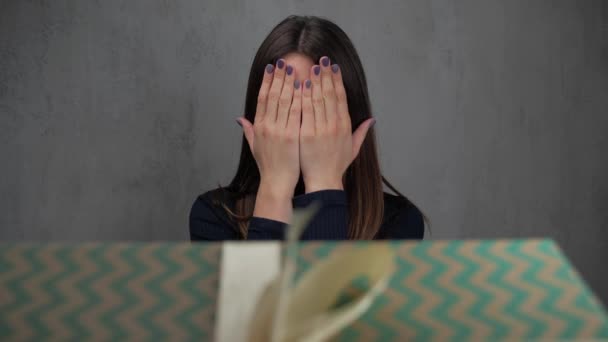 Une jeune femme se tient les yeux fermés, les ouvrant elle voit une boîte avec un cadeau. Fond gris, ralenti. 4k . — Video