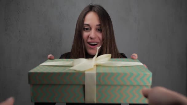 Una joven está de pie con los ojos cerrados, abriéndolos, ve una caja con un regalo. La chica desempaca la caja y se sorprende. cámara lenta 4k . — Vídeo de stock