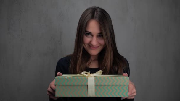 Zbliżenie młody szczęśliwy uśmiechnięta kobieta dając pudełko prezent. Szare tło. 4K — Wideo stockowe