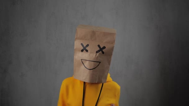 Cute girl in a yellow sweatshirt puts a paper bag over her head and dancing. 4k — Stock Video