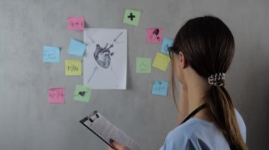 Gözlüklü güzel bir kadın doktor öğrencinin portresi arka planda bir sunum hazırlıyor. Genç kadın çizer ve kağıt üzerinde notlar. Kavram: fikirler, bilim, öğretmen, bellek, biyoloji,