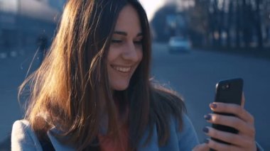 Yakın portre genç kadın güneşli şehir sokaklarında yürüyüş , cep telefonu kullanarak neşeli kız, gün batımı arka plan.