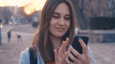 Çekici genç kadın güneşli şehir sokaklarında yürüyüş ve arkadaşları ile sohbet, cep telefonu açık havada kullanarak, gün batımı arka plan