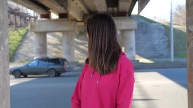 Köprünün altında şehrin arka planında ahududu sweatshirt genç bir kadının portresi. 4k