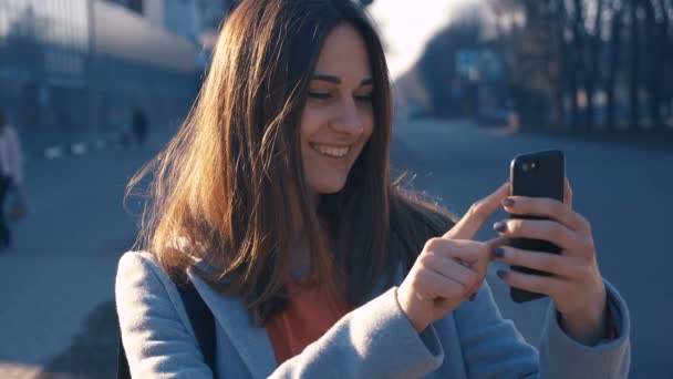 Привлекательная молодая женщина, гуляющая по солнечным улицам города, радостная девушка с сотовым телефоном, закат фон . — стоковое видео