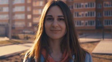 Bir apartmanın arka planına doğru gülümseyen genç bir kızın yakın çekim portresi. Gün batımı ve sıcak bir flaş kadın yüzünde dolaşmak.