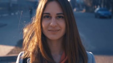 yakın çekim portre genç kız şehir arka plan üzerinde gülümseyen. Gün batımı ve sıcak parlama kadın yüzü üzerinde dolaşmak vardır.