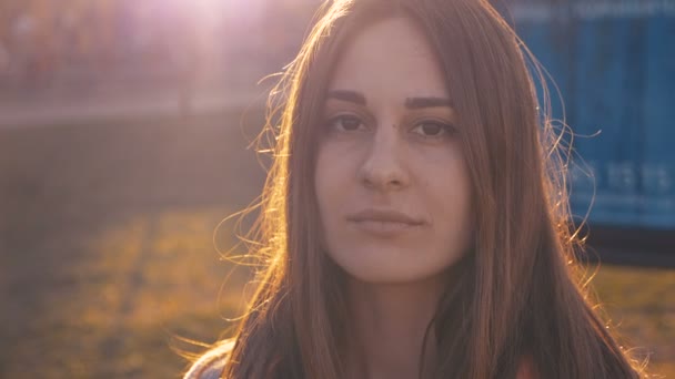 Primer plano retrato de la joven sonriendo con el pelo castaño oscuro soplando en el viento mirando el atardecer. — Vídeos de Stock