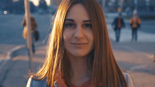 Primer plano retrato chica joven sonriendo sobre fondo de la ciudad. La puesta del sol y la llamarada caliente vagan sobre la cara de la mujer . — Vídeo de stock