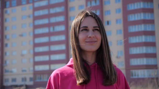 Portrait of a dark-haired brunette in a city on background residential building. Girl smiles and her hair develops in the wind. the suns rays and a warm flash roam the feminine face. 4k — Stock Video