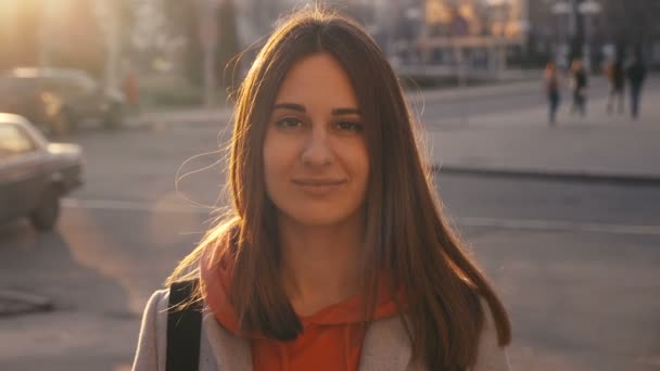 Zaostřená portrét mladé dívky usmívající se na pozadí města. Slunce a vlažné erupce se potulují po ženské tváři. — Stock video