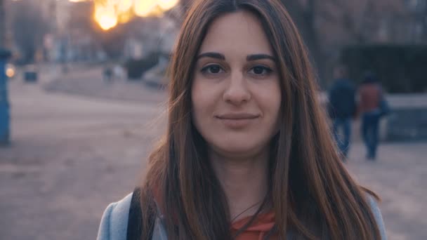 Zaostřená portrét mladé dívky usmívající se na pozadí města. Slunce a vlažné erupce se potulují po ženské tváři. — Stock video