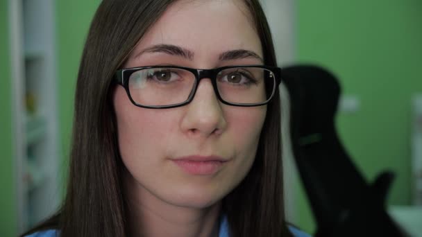 Primer plano retrato de mujer joven con gafas mirando a la cámara seria en el interior de trabajo. En cámara lenta. 4k — Vídeos de Stock