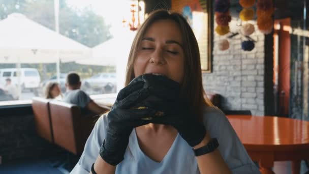 Голодная девушка ест черный бургер в ресторане быстрого питания. 4K Slowmotion . — стоковое видео