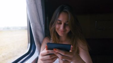 Pensive kadın rahatlatıcı ve bir tren penceresinden dışarı bakıyor ve kitap okuma. Yan görünüm. Seyahat, ulaşım konsepti