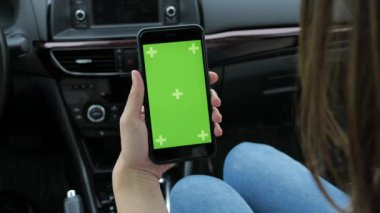Bir kadın yeşil arka planlı bir telefon kullanıyor. Arabada oturuyor.