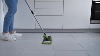 Beyaz mutfak zeminini sprey boyayla yıkayan kadın, temizlik servisi, yakın çekim.