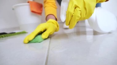 Sarı eldivenli ev hanımı beyaz zemini köpük ve süngerle temizlemeye çalışıyor.