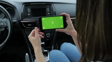 Bir kadın yeşil arka planlı bir telefon kullanıyor. Arabada oturuyor.