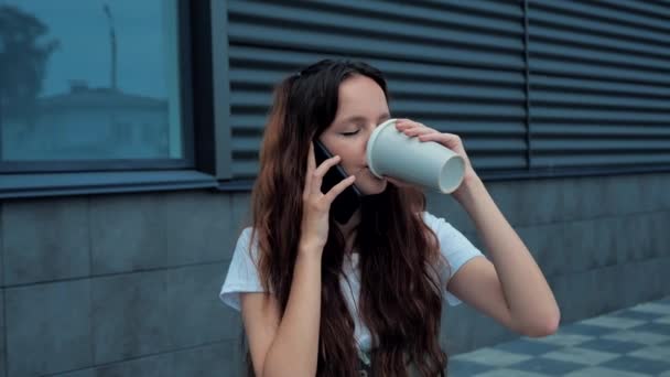 Genç iş kadını cep telefonuyla konuşuyor. Genç ve mutlu bir bayan cep telefonuyla konuşuyor ve ofis 4K yakınlarında kahve içiyor. — Stok video
