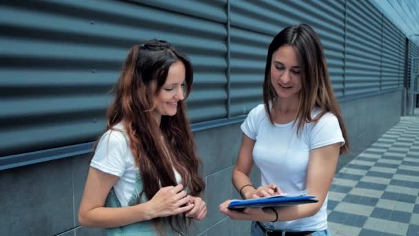 Duas jovens mulheres discutem um projeto de trabalho em pé na rua até o centro de negócios. 4K. — Vídeo de Stock