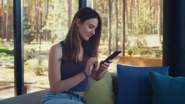 Entspannte junge Frau ohne Gesicht surft mit dem Smartphone in den sozialen Medien, checkt Nachrichten, spielt Handyspiele oder schreibt SMS auf dem Sofa. — Stockvideo