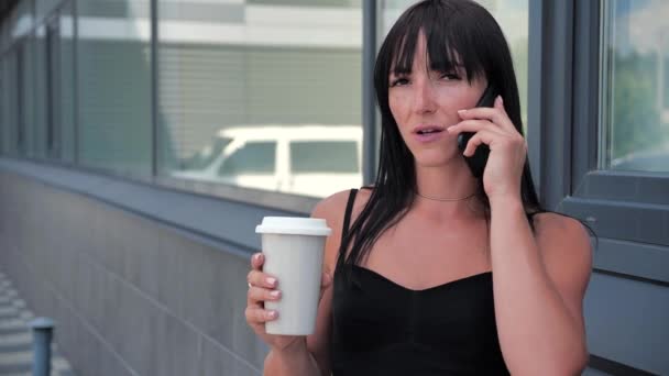 Mujer hablando por celular y tomando café cerca del centro de negocios, cámara lenta 4k — Vídeos de Stock